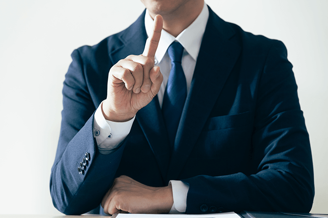 スーツ姿の人物が人差し指を立て、ポイントを示している様子