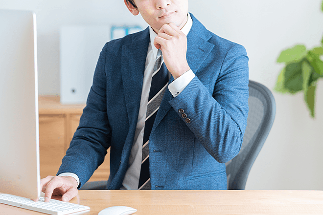 ノートパソコンを操作しながら、手元の書類を確認している人物の手元