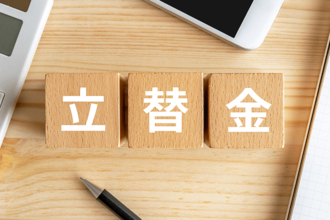 木製ブロックに「立替金」と書かれ、周囲に電卓とノートが見えるイメージ画像